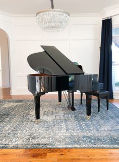 a grand piano in a living room with chandelier and blue rug on the floor