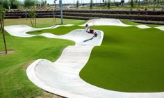 a skateboarder is riding down a ramp in a park with artificial grass on the ground