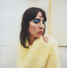 a woman with bright blue eyes and long hair wearing a yellow sweater is posing for the camera