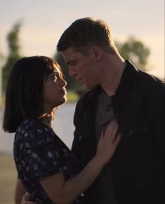 a man and woman standing next to each other in front of a body of water