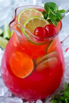 a pitcher filled with liquid and garnished with limes, cherries and lemon wedges