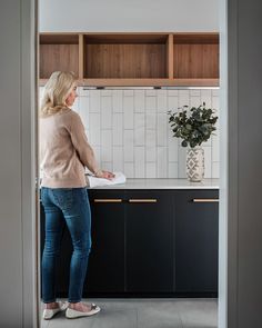 a woman is standing in the kitchen and looking at something on the counter top that she is holding