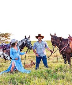 a man and woman standing next to two horses in a field with a dog on the other side