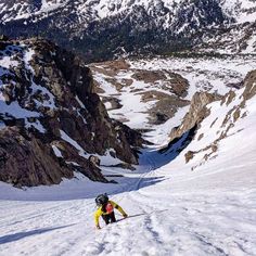 two skiers are skiing down a snowy mountain slope with mountains in the back ground