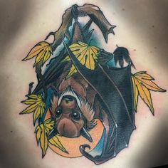 a woman's back with a bat and leaves tattoo on her shoulder, which is decorated with yellow leaves