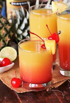 two glasses filled with orange and red liquid next to pineapples on a table