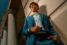 a man in a blue suit and tie standing next to a tall building with columns