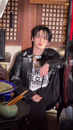 a young man sitting in a chair wearing a leather jacket and looking at his watch