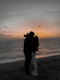 two people standing on the beach at sunset