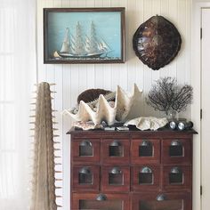 a cabinet with shells and seashells on it in front of a wall hanging