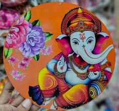 a hand holding an orange plate with a painting of ganeshi on the front