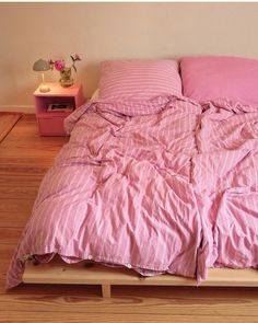 a bed with pink sheets and pillows on top of wooden floor next to nightstands