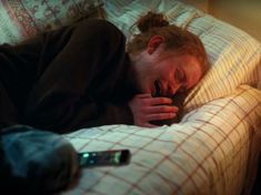 a woman laying in bed with her head on the pillow while holding a cell phone