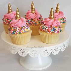 three cupcakes with pink frosting and sprinkles on a cake plate