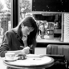 a woman sitting at a table with a pen in her mouth