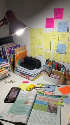 a cluttered desk with lots of papers and notes on it, including a cell phone