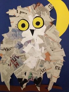 an owl made out of newspaper sitting on top of a wooden table next to a half moon