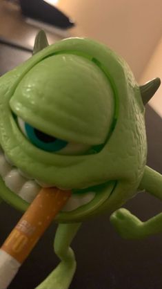 a green toy with an orange pencil in it's mouth