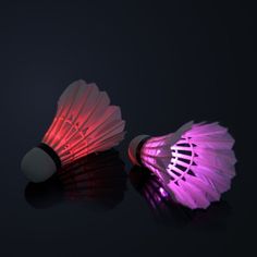 two light up fan shaped objects on a black surface, one is pink and the other is white