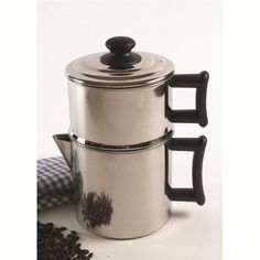 two stainless steel pots with black handles and spoons next to coffee beans on a white surface