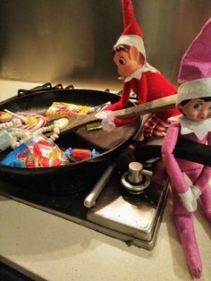 two elfs sitting on top of a stove next to a pan filled with candy