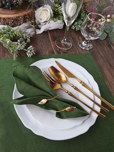 a place setting with green napkins and gold utensils on a wooden table