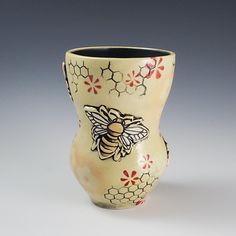 a ceramic vase with bees and flowers painted on the outside, sitting on a white surface