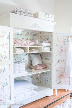 a white closet filled with lots of pillows and blankets next to a wallpapered wall