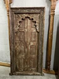 an old wooden door with carved designs on it's sides and pillars in the background