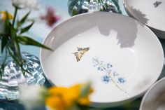 a plate with a butterfly on it sitting next to flowers and vases in the background