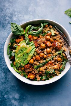 a white bowl filled with vegetables and meat on top of a blue countertop next to a fork