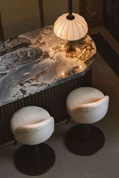 two white stools sitting next to a table with a lamp on top of it