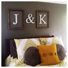 a bed with pillows and two framed initials on the wall above it's headboard