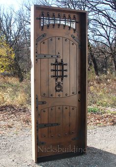 an open wooden door in the middle of a dirt area with trees and bushes behind it