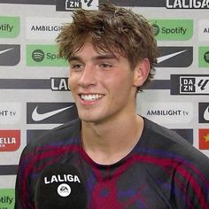 a young man standing in front of a wall with logos on it and smiling at the camera