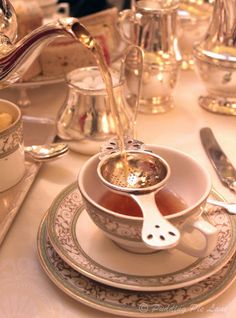 tea being poured into a cup on top of a plate with silverware next to it