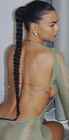 a woman sitting on the floor with her back turned to the camera, wearing a fishtail braid