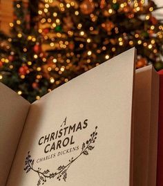 an open christmas carol book sitting in front of a christmas tree