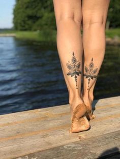 a woman's legs with tattoos on them standing on a dock next to the water