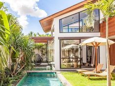 an outdoor swimming pool in front of a house with palm trees and lawn chairs next to it