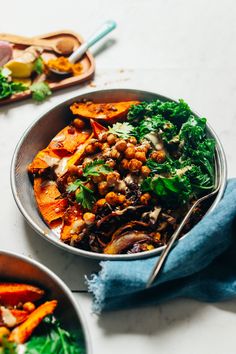 two bowls filled with food on top of a white table next to wooden spoons