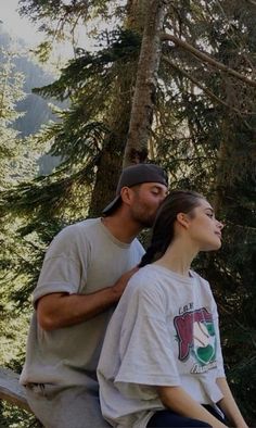 a man and woman are sitting on a bench in the woods, looking up into the sky