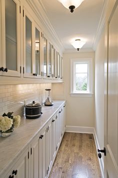 a kitchen with white cabinets and wood flooring next to a window on the wall