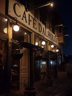 the outside of a restaurant at night with lights on and signs above it that read cafe dalhousee