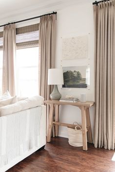 a white bed sitting next to a wooden table in a room with curtains on the windows