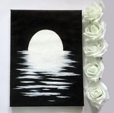 white roses are next to a black and white painting with the moon in the background