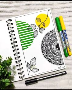 an open spiral notebook with green and yellow designs on it next to two markers, some plants and a potted plant