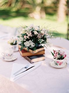 a table topped with books and flowers on top of a white cloth covered tablecloth