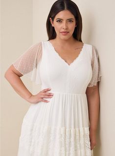 a woman standing in front of a wall wearing a white dress