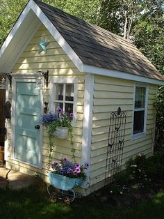 a small yellow house with flower pots on the front door and window boxes in the back